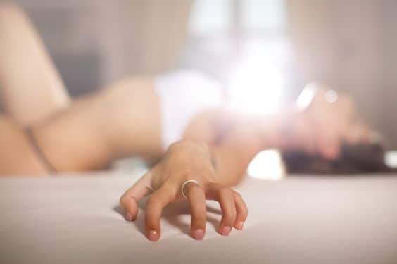 Mulher deitada na cama usando um brinquedo sexual e tendo um orgasmo