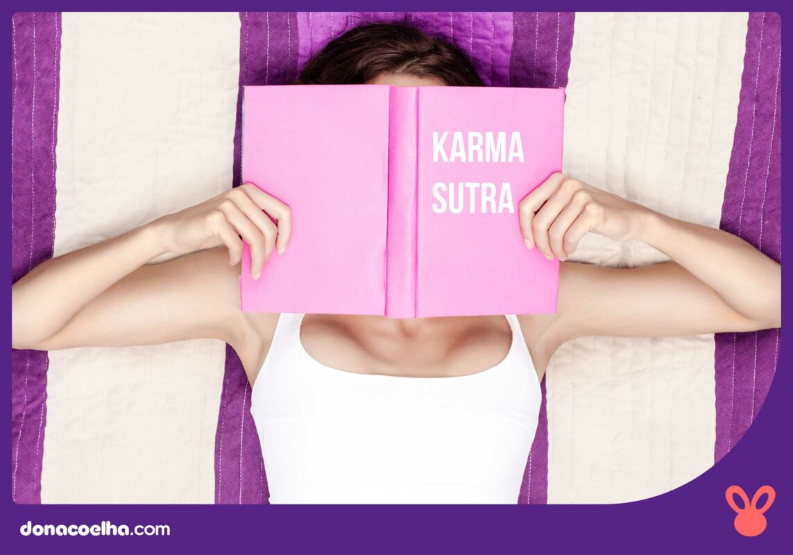 Mulher deitada em uma cama lendo um livro rosa com o título Kama Sutra
