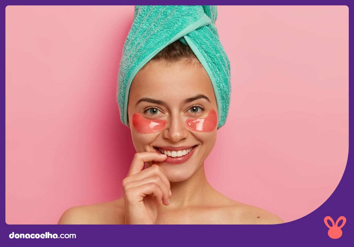 Mulher sorrindo para a foto com o cabelo enrolado na toalha e usando itens de beleza nor rosto