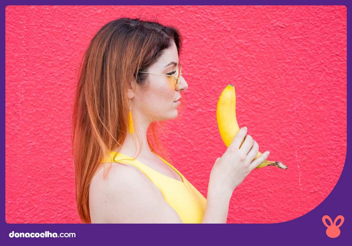 Pessoa vestindo uma regata amarela, de lado, segurando uma banana